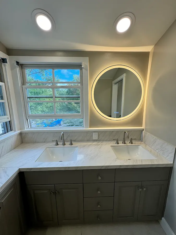 Bathroom vanity with marble countertop and an illuminated round mirror